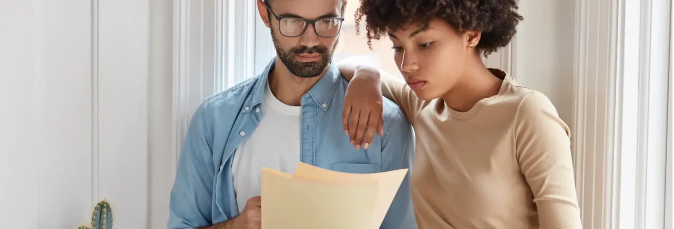 Homem de óculos e uma mulher lendo atentamente regulamento impresso de promoção realizada pela MRV