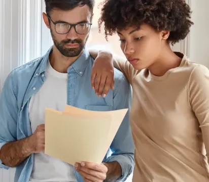 Homem de óculos e uma mulher lendo atentamente regulamento impresso de promoção realizada pela MRV